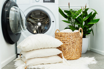 Laundry basket and pile of white pillows in front of the opened washing machine in laundry room....