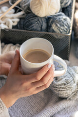 A cup of coffee in female hands and a thread of yarn.