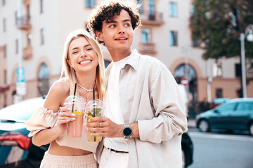 Young smiling beautiful woman and her handsome boyfriend in casual summer clothes. Happy cheerful family. Female having fun. Couple posing in street. Holding and drinking cocktail drink in plastic cup