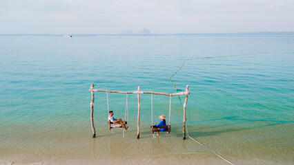 a couple of men and woman on a swing at the beach of Koh Muk Thailand