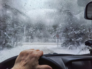 Hand of woman on steering wheel in car and and the forest with cloudy windshield, fogged with snow ice in winter. Blurred woman driving car in travel