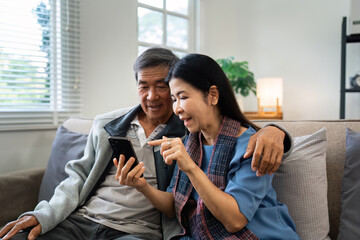 Retired elderly couple sits on couch drink tea and using mobile together and relax in their home. Senior Activity Concept