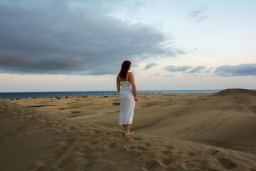 Young woman stands with her back in the sand dunes