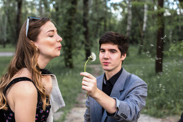 Fototapeta premium Portrait of young couple in love blowing dandelion in the park