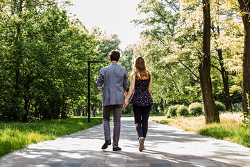 Fototapeta premium Back view of a young couple walking in the park on a sunny day
