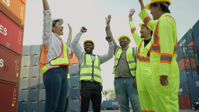 Multiracial team of engineer and foreman in hardhat and safety uniform stacking hands and cheering to celebrate after finishing job at container yard warehouse shipping port. Successful teamwork