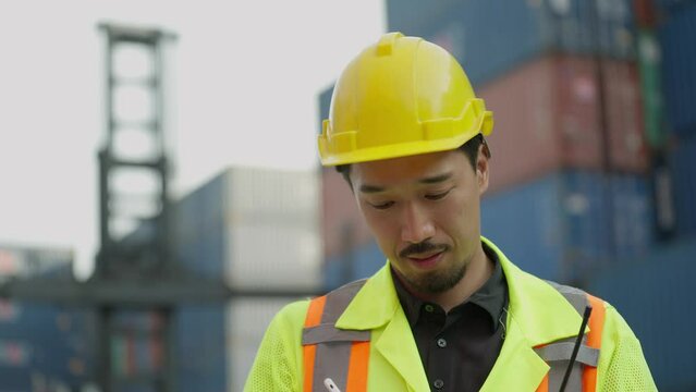 Young asian japanese foreman in hardhat and safety uniform working on tablet checking inventory cargo container at industrial yard. Foreman working at container cargo. Logistic concept 