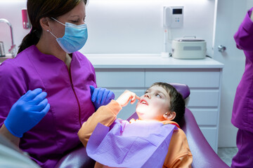Boy at the dentist's office lying in the dentist's chair explaining which tooth hurts to the dentist