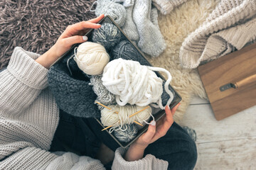 Close-up woman hands wearing in a wool sweater holding box with balls of thread.