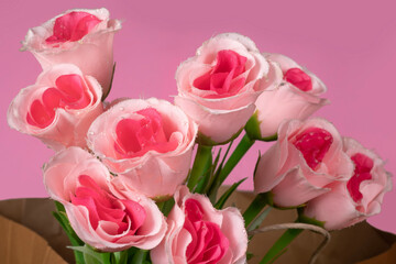 Beautiful bouquet of pink roses in paper bag on pink background, Closeup