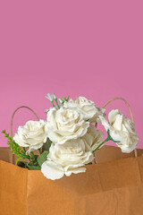 Bouquet of white roses in a paper bag on a pink background, valentine's day background