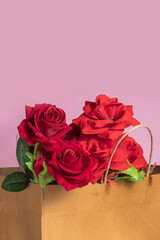 Bouquet of Red roses in a paper bag on a pink background with copy space