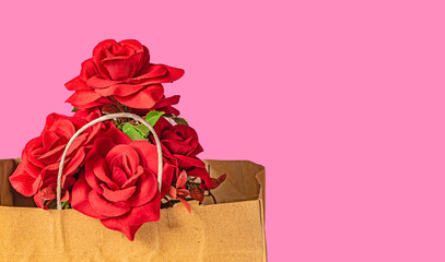 Bouquet of red roses in a brown paper bag on a pink background for Valentine's Day with copy space for your text.