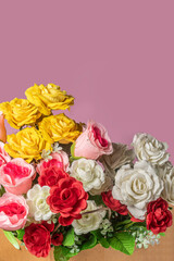Bouquet of colorful artificial flowers in paper box on pink background with copy space.