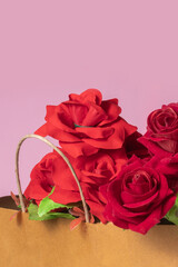 Bouquet of red roses in brown paper bag on pink background for Valentine's Day celebration