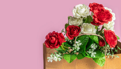 Bouquet of white and red artificial roses in a brown paper bag on a pink background