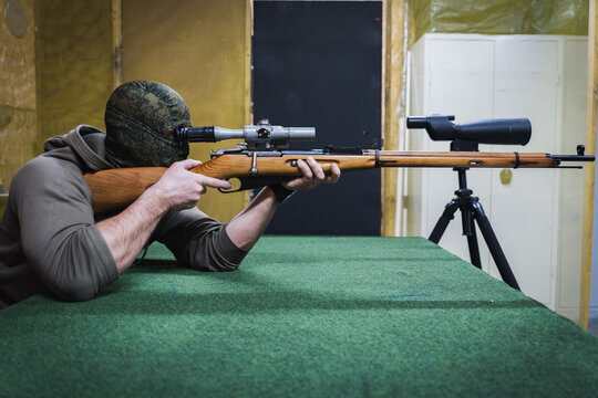 Male sniper with a classic bolt action rifle at a shooting range.