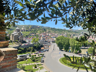 Cute landscape of Tbilisi city center with old city on the background of sky and green laves on front view