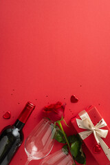 Classic love scene. Top view vertical snapshot of a pair of wineglasses, wine, a rose, heart decorations, and sequins on a red background, offering a gap for textual content or advertising
