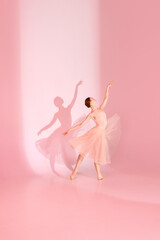 Elegant Pose. Ballerina in pink traditional ballet dress, tutu poses barefoot against pastel pink...