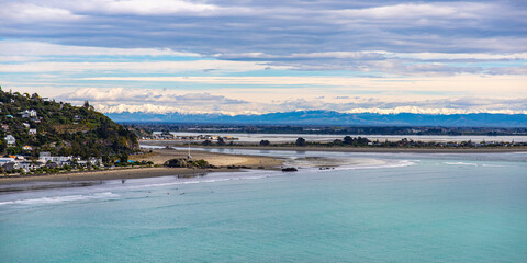 panorama of famous sumner beach in christchurch, canterbury, new zealand; beautiful beach with christchurch city and snow covered mountains in the background