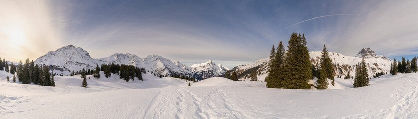 Panoramic view, Panorama view with snowy mountains in Bregenzerwald, Austria, Körber lake with brown Arlberg peak and river in snowfield, trees and sky with veil clouds