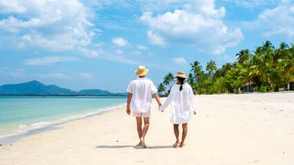 Koh Mook a young couple of caucasian men and Thai Asian woman walking at the beach in Thailand