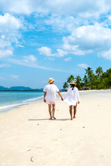 Koh Mook a young couple of caucasian men and Thai Asian woman walking at the beach in Thailand