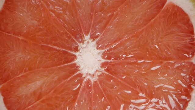Macro zoom, a half of a grapefruit with red juicy flesh on a wooden table. Dolly slider.