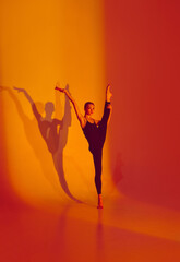 Graceful Ballet in Neon Light. Athletic and flexible woman, ballet dancer in black overalls, dances barefoot against gradient background, shadow in motion. Concept of athleticism, grace, movement.