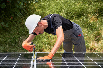 Man in safety helmet building photovoltaic solar panels outdoors. Male worker in work gloves...