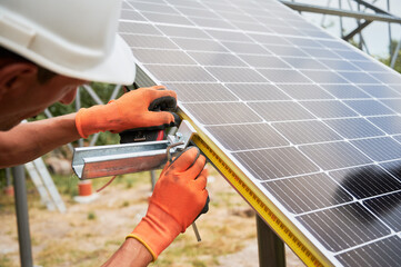 Worker measuring solar panel with measuring tape while installing this panel on metal beams....