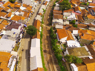Bird's eye view from drone of a railroad track between residential areas and rice fields in Cicalengka, Indonesia. Shot from a drone flying 200 meters high.