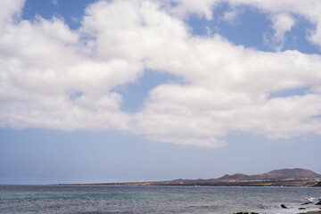 Seascape. Large white clouds. Mountains in the background. Rocky beach, turquoise Atlantic Ocean. Village of Arrieta. Lanzarote, Canary Islands, Spain