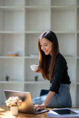 Smiling businesswoman holding a cup of coffee while working on her laptop in a contemporary office space..