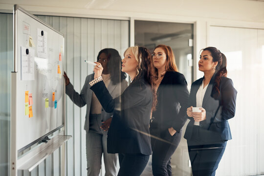 Group of diverse businesswomen brainstorming on a whiteboard in a boardroom