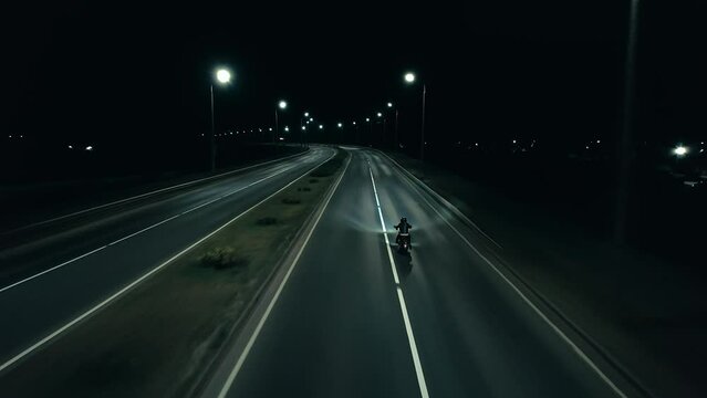 Aerial view of man in black helmet and black leather jacket riding motorcycle on deserted night highway