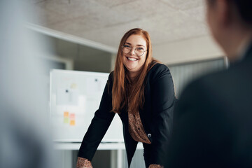 Young red head businesswoman laughing while giving a presentation to coworkers in an office