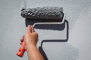 Pintor de rolo na mão a pintar uma parede exterior