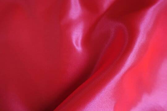 Soft fold on vibrant reddish pink satin polyester fabric