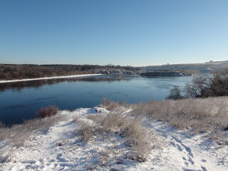 A view from the high rocky bank of the Dnieper to the snowy island of Khortytsia under a clear blue sky.