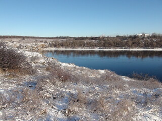A view from the high rocky bank of the Dnieper to the snowy island of Khortytsia under a clear blue sky.