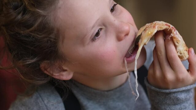 Stylish child boy is eating cheese pizza with pleasure