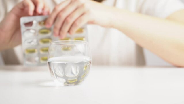 Close-up hands of woman remove a medicine tablet from a blister pack. Taking pills, tablets, capsules with omega 3. Vitamin supplements for health.
