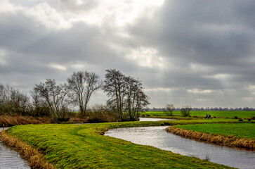 Polder landscape with canals and meadows with two anglers under a dramatic sky near Schoonhoven, The Netherlands
