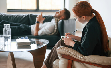 Lying down on the sofa. Man is on the therapy session with female psychologist