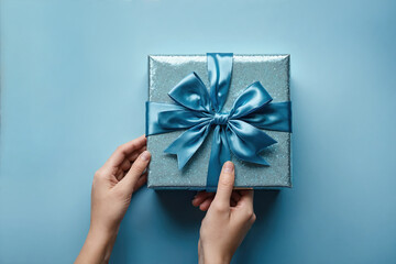 A woman's hands hold a blue gift box with a blue bow.