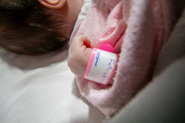 On her first day of life, a newborn baby girl wears a pink hospital ID bracelet on her hand - obrazy, fototapety, plakaty