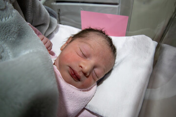 On her first day of life, a newborn baby girl wears a pink hospital ID bracelet on her hand