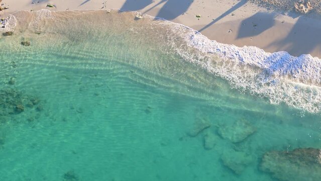 Ocean waves roll up on golden sand shores at early morning in Caribbean paradise